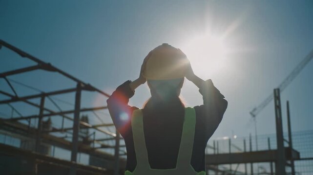 強烈な夏の日差しのもと屋外作業中に頭を抱える作業員のシルエット