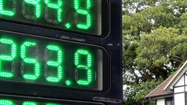 Close-up slow pan left and downward across a roadside fuel price sign displaying high petrol and diesel costs. Large numeric pricing dominates the frame, clearly communicating rising fuel prices 