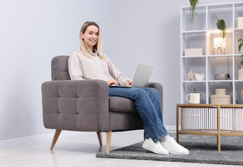 Obraz premium Woman using laptop in armchair at home
