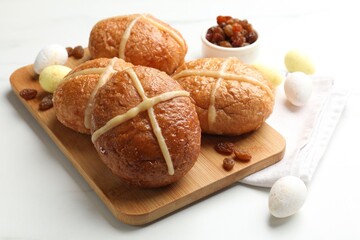 Hot cross buns, raisins and decorated eggs on white table, closeup