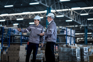 Fototapeta premium Professional industrial managers wearing safety uniform communicating while walking in factory storehouse. Male logistics team planning safe commercial freight delivery operations.