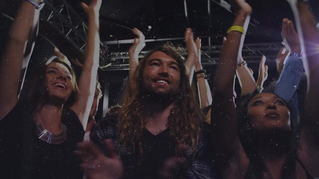 Three foreground concertgoers reacting to music performance, raising arms and clapping under lights