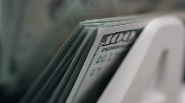 Close-up of a stack of $100 bills being counted in a money counter. Finance, banking, and cash flow concept.
