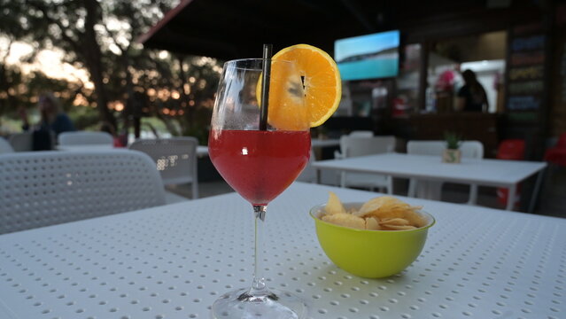 cocktail alcolico rosso in un bicchiere con una fetta d'arancia servito in una pineta vicino al mare in una sera d'estate