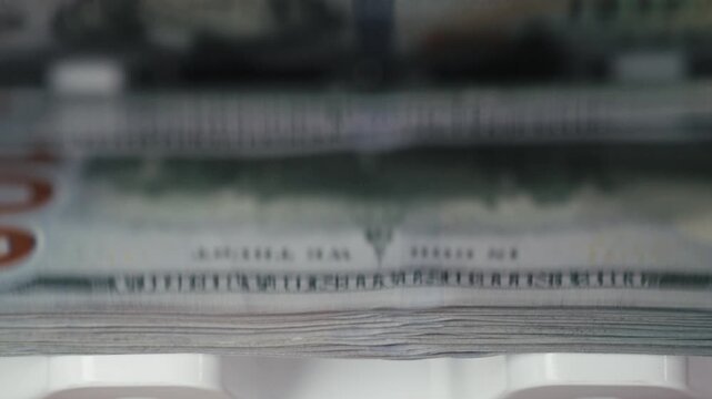 Close-up of $100 bills running through a modern money counting machine. Finance and banking concept.

