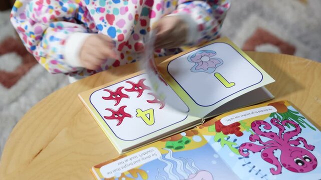 Cute little girl with educational books at wooden table indoors, closeup. Camera moving forward