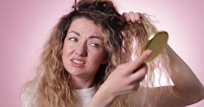 Unhappy woman trying to brush her tangled hair on pink background