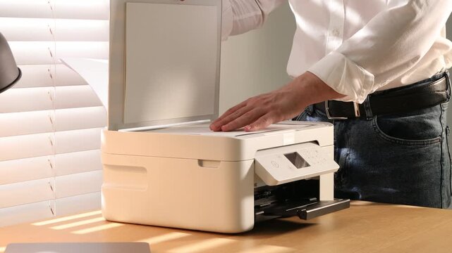 Man working with printer at wooden desk indoors, closeup