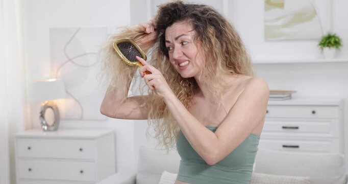 Unhappy woman trying to brush her tangled hair at home
