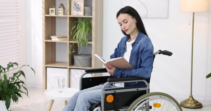 Woman in wheelchair reading book and drinking water at home