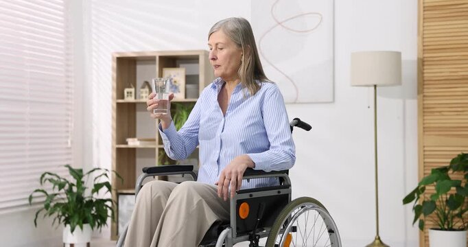 Senior woman in wheelchair drinking water at home