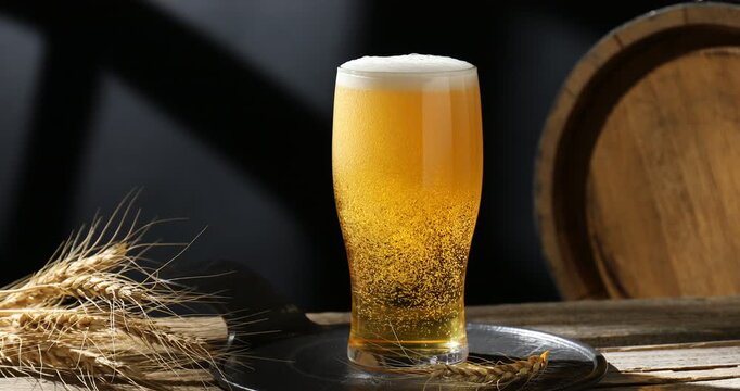 Pouring fresh beer into glass at wooden table, spikes and barrel against black background, closeup