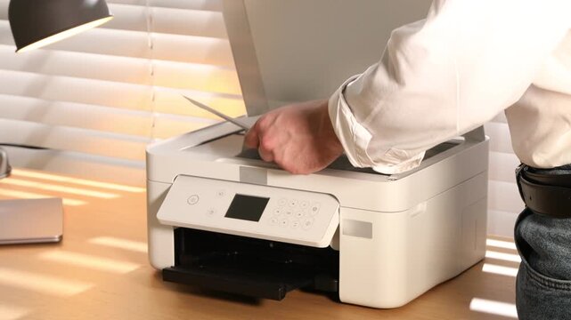 Man working with printer at wooden desk indoors, closeup