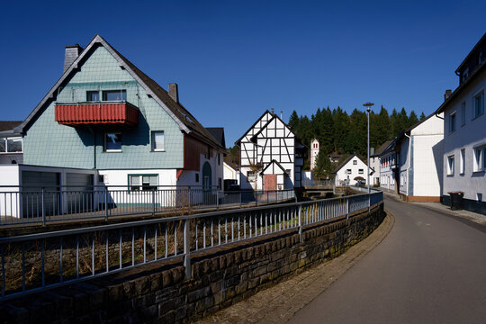 Scenic view of a quiet street in Hellenthal, Germany. Featuring half-timbered houses, slate facades, and a clear blue sky in the Eifel region.