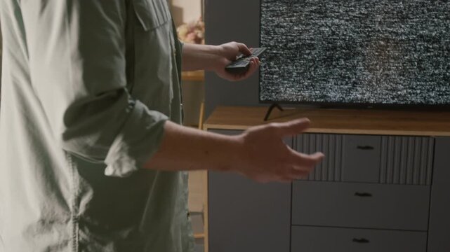 Tilting medium close-up of angry young Caucasian man standing by broken TV set with static noise on screen, gesticulating while arguing, with genuine dismay and frustration over service disruption