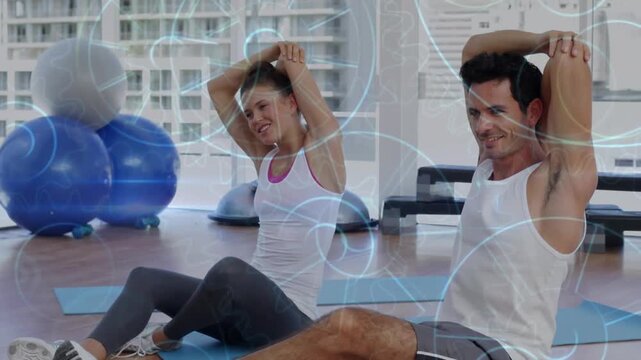Fitness duo on blue mats raising arms on cue leaning twisting warming while circles appearing