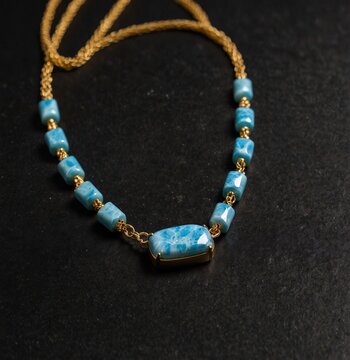 Radiant cut larimar gemstone on gold necklace on plain black background