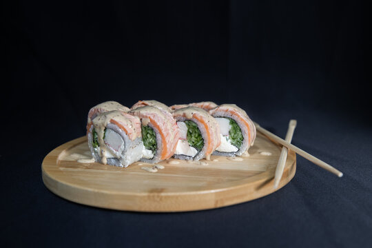Sushi roll with salmon, cheese and avocado. Maki roll with shrimps fried, avocado and lattuce on a wooden plate . Delicious sushi rolls served on grey table