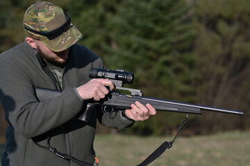 Fototapeta premium Hunter adjusting scope on a bolt-action rifle at a woodland shooting range during daytime