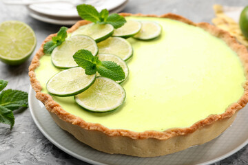 Tasty lime pie with fruit slices and mint leaves on grey textured table, closeup © New Africa