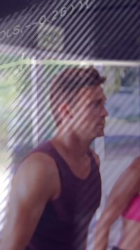 Vertical video: Man in tank after coach cue raising arms for group fitness with chart over group