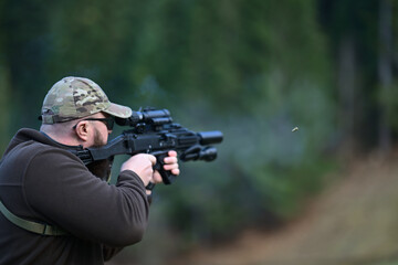 Fototapeta premium Man in camouflage cap aiming rifle at outdoor shooting range with spent shell ejecting
