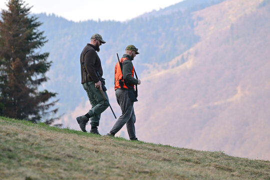 Two hunters walking down a mountain slope carrying rifles during autumn hunting trip