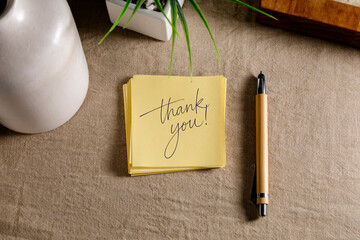 Thank you message on yellow sticky note with pen on desk, gratitude and appreciation concept.