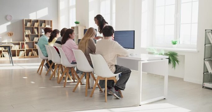Students and teacher in classroom computer training. Teenagers collaborate at desktops as the teacher guides projects in a lab for education. Teamwork and digital learning success concept.
