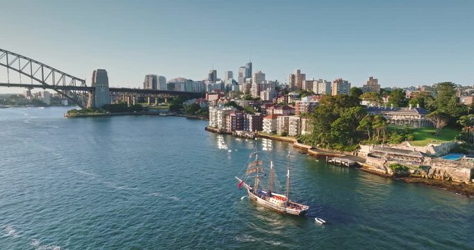 Wooden tourist ship navigating through Sydney Harbour, offering a scenic view of the iconic Sydney Harbour Bridge, the Kirribilli shoreline, and the bustling city skyline in Australia. Aerial flight