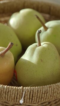 Close-up cinematic panning shot of several fresh ripe asian pears in natural light in a woven basket