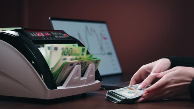 Unrecognizable female analyst counting cash in money counting machine with financial chart on laptop. Business and finance concept.
