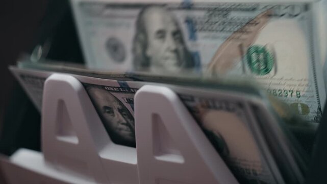 Close-up of one hundred dollar banknotes in automatic money counting machine. Banking and finance concept.
