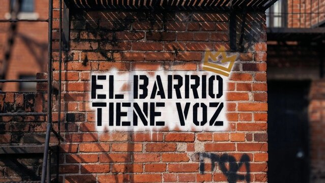 Graffiti con plantilla "El barrio tiene voz" en pared de ladrillo roja con escalera de incendios.