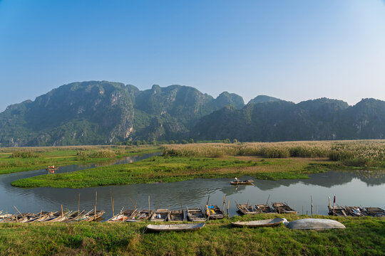Wide river scene with small boats and winding waterway through green wetlands surrounded by limestone mountains in Van Long Ninh Binh.