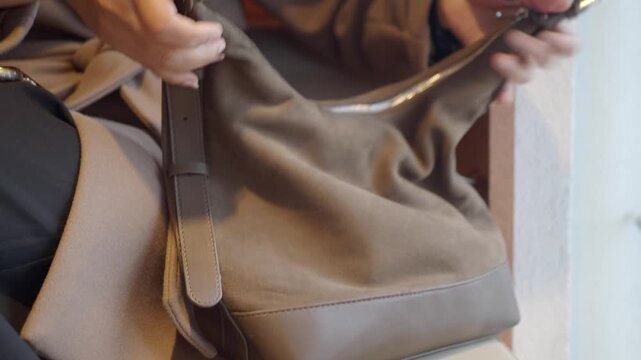 Woman's hands opening a stylish brown suede handbag and searching inside