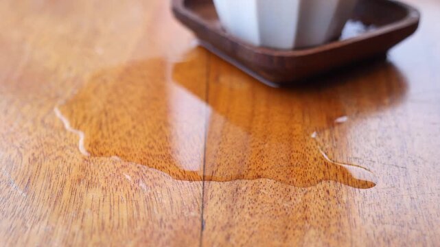 Close up of spilled water puddle on wooden table surface near small white ceramic cup on coaster