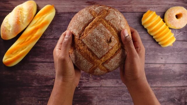 Baker holds fresh bread surrounded by various baked goods