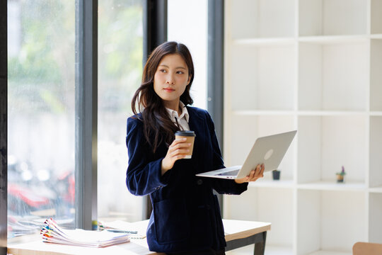 A woman thoughtfully gazes at her laptop in a sleek office, embodying determination and strategic thinking in a contemporary business environment.