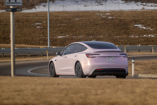 Calgary, Alberta, Canada. March 19, 2026. Rear Three-Quarter View of a Pink Tesla Model 3 Electric Car Driving on a Curved Highway Road.