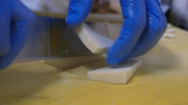 Detail of a sharp knife cutting a slice of cheese.