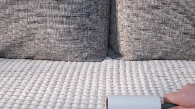 A woman's hand cleaning a sofa with a sticky roller, close-up.