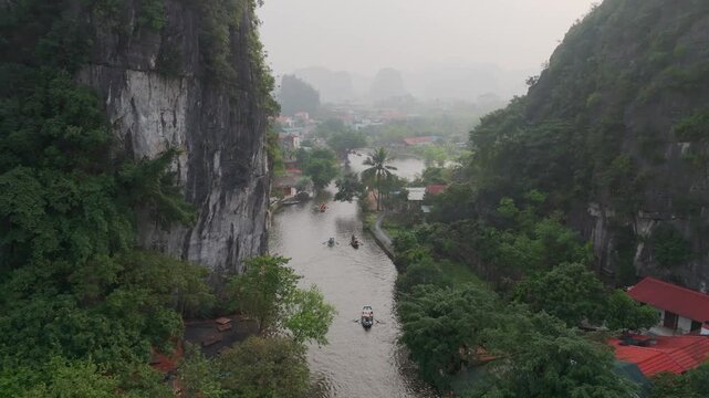 Aerial view of Tam Coc river winding between dramatic limestone karst cliffs with small boats carrying tourists through lush green landscape in Ninh Binh Vietnam