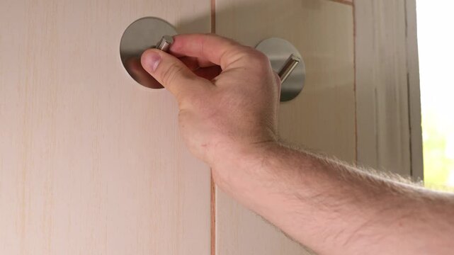 A man sticks a metal hook on tiles and hangs a purple towel. Male hands install a self-adhesive hook on a tiled kitchen wall and then hang a kitchen towel on it