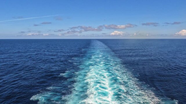 Luxury cruise ship gliding across the calm open sea, leaving white ocean trails beneath a bright blue sky during late afternoon hours.