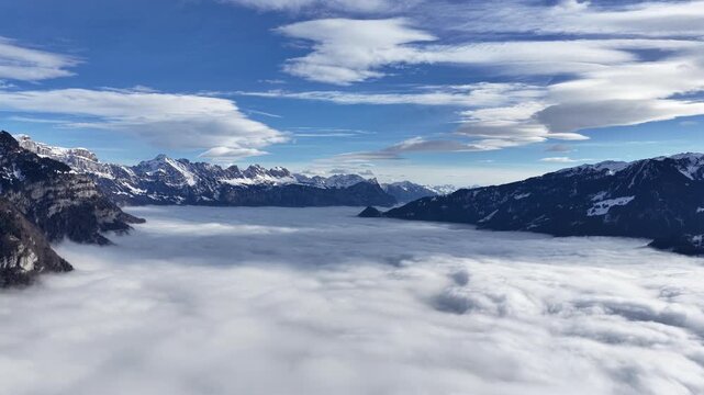 Snow-covered alpine mountains surrounding dense cloud inversion beneath blue sky, Walensee region, Switzerland