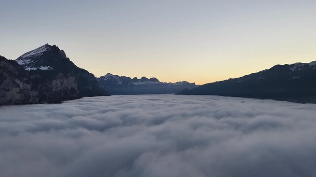 Thick cloud inversion filling alpine valley between dark mountain ridges at dawn, Walensee region, Switzerland