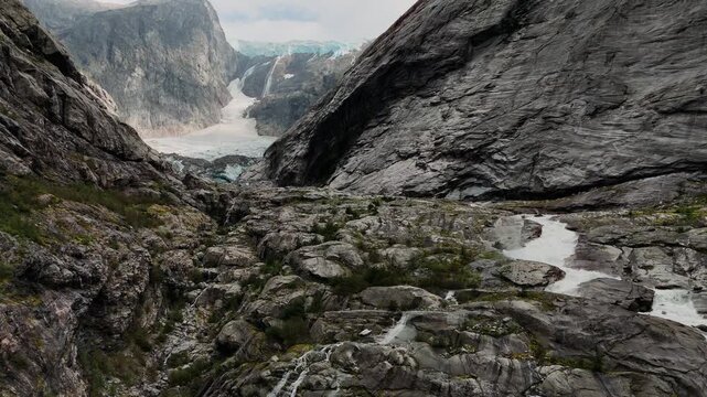 Ice flow through dramatic gorge with vertical cliffs and milky meltwater river below, Norway mountains