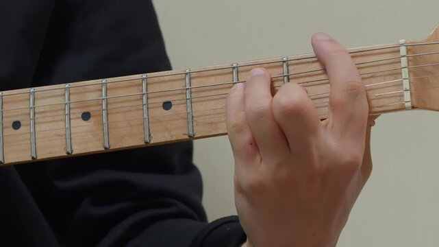 A close-up shot of a musician's hand changing chords on the maple fretboard of an electric guitar. The player demonstrates finger placement and technique while playing,
