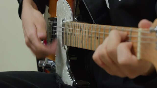 Close-up video of a musician's hands playing an electric guitar. The guitarist strums the strings with a pick and frets notes on the maple neck. Focus on musical performance and technique.